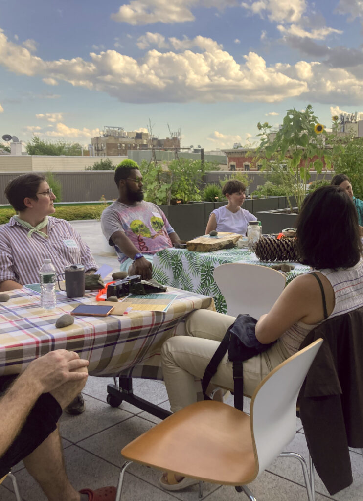 A group of people sitting around a table on a rooftop talking to one another.